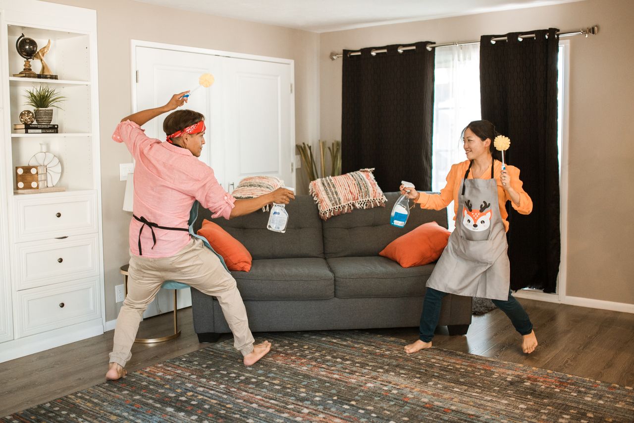 A cheerful couple shares a playful cleaning tussle in their living room, highlighting a light and happy home life.
